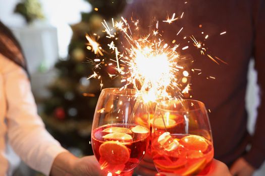 Close-up of people raise fire sparklers and glass filled with champagne and celebrate winter holiday together. Party, nightlife, new year, festive concept