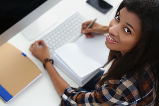 Top view of smiling afro american young woman on workplace, open journal, luxury pc device on desk. Fresh start, mockup, copy space, technology concept