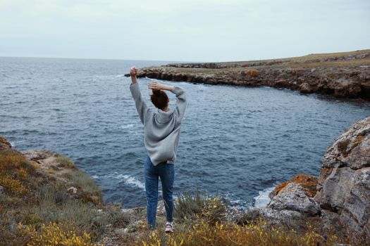 pretty woman in a gray sweater stands on a rocky shore nature Relaxation concept. High quality photo