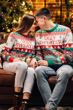 Surprised wife receiving christmas gift from loving husband at home on Christmas Eve near decorated glowing tree. Caucasian man giving present to beloved woman on holidays. Family celebration.