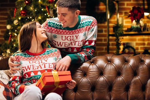 Happy man is making christmas gift to his beloved woman. Woman is surprised and excited after opening received gift box. Concept of holidays, romance, surprise, xmas. Holiday miracle. Merry Christmas