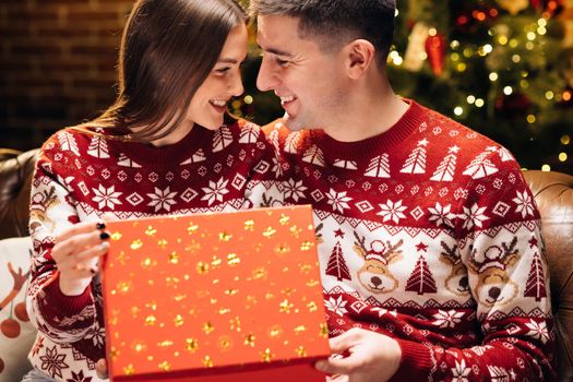 Happy man is making christmas gift to his beloved woman. Woman is surprised and excited after opening received gift box. Concept of holidays, romance, surprise. Holiday miracle.