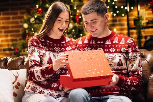 Woman is surprised and excited after opening received gift box. Happy man is making christmas gift to his beloved woman. Concept of holidays, romance, surprise. Holiday miracle.