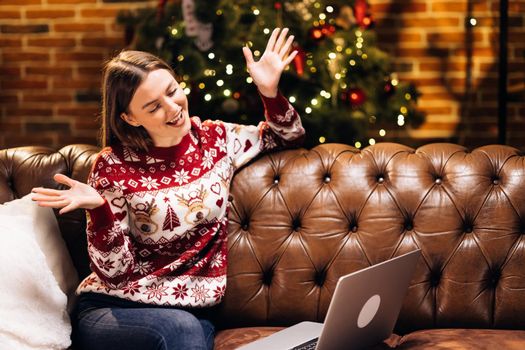 New Year greetings for you. Happy young woman relax on couch use laptop celebrate Xmas with online friend in conference app. Teen biracial female make Christmas speech by video call