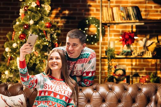 Happy caucasian man and woman couple at home with decorated christmas tree online video chatting and saying holiday greetings to friends and relatives. Xmas eve. Holidays spirit