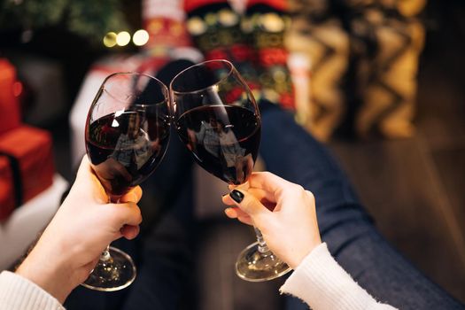 Happy couple clink wine glasses toast and celebrate together New 2022 Year at home near glowing Christmas tree. Wine for christmas and new year celebrations. Congratulations concept