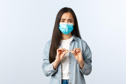 Social distancing lifestyle, covid-19 pandemic everyday life and leisure concept. Sick asian girl test positive coronavirus, measure temperature, holding thermometer, wear medical mask, have fever.