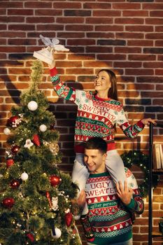 Happy couple preparing for New Year winter holidays celebration concept. Young 30s couple decorating Christmas tree create festive mood atmosphere at modern cozy house