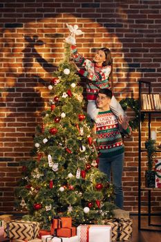 Happy couple preparing for New Year winter holidays celebration concept. Young couple decorating Christmas tree create festive mood atmosphere at modern cozy house.