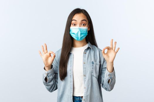 Social distancing lifestyle, covid-19 pandemic everyday life and leisure concept. Excited impressed asian female in medical mask showing okay signs in approval, customer recommend shop.