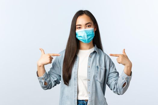 Social distancing lifestyle, covid-19 pandemic everyday life and leisure concept. Serious professional IT freelancer, female asian girl in medical mask pointing herself, promote own service.