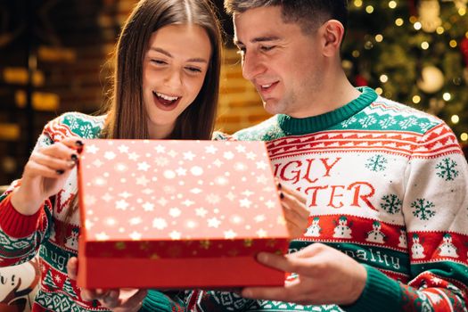 Happy man is making christmas gift to his beloved woman. The woman is surprised and excited after opening received gift box. Concept of holidays, romance, surprise, e-commerce, Xmas, Holiday miracle.