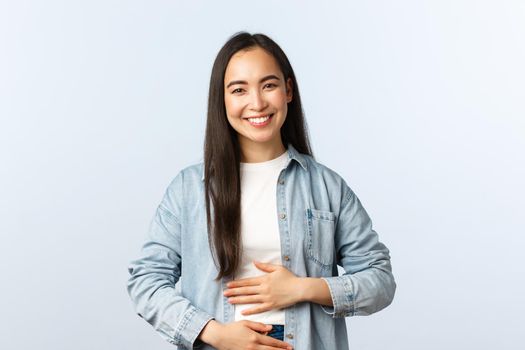 Lifestyle, people emotions and beauty concept. Pleased smiling asian woman rubbing her belly, being full after eating, pleased feeling in stomach from drinking yoghurt.