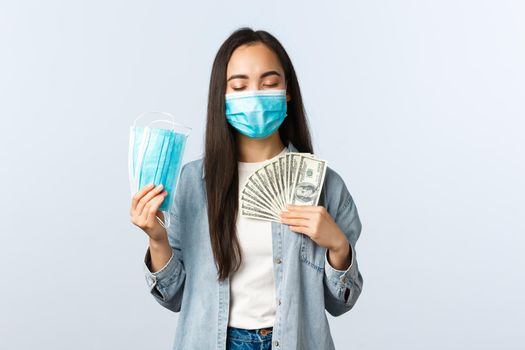 covid-19 pandemic, coronavirus expences and finance concept. Satisfied greedy asian girl in medical mask hugging money and showing masks, earn cash during coronavirus lockdown.