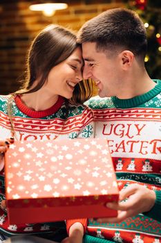 Happy man is making christmas gift to his beloved woman. The woman is surprised and excited after opening received gift box. Concept of holidays, romance, surprise, e-commerce, Xmas, Holiday miracle.