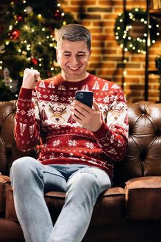 Joyful caucasian young happy man smiling with surprised face tapping on cell phone feeling excited and happy winning christmas lottery. Xmas concept. Holiday miracle. Merry Christmas