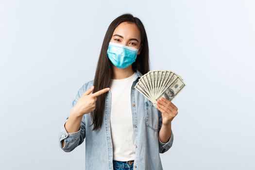 Social distancing lifestyle, covid-19 pandemic business and employement concept. Young happy asian female freelancer working from home on coronavirus, point at money dollars.
