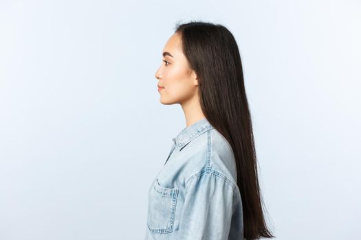 Lifestyle, people emotions and beauty concept. Profile of beautiful korean girl with long dark hair looking left, standing straight in casual clothes, visit hairdresser beauty salon.