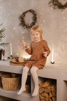 A girl is playing on Christmas Eve in a beautiful house decorated for the New Year holidays. Scandinavian-style interior with live fir trees and a wooden staircase.