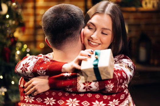 Close up of caucasian family embracing standing near decorated glowing fir tree. Happy wife feels grateful hugs husband express gratitude for New Year gift. Christmas holidays celebration concept.