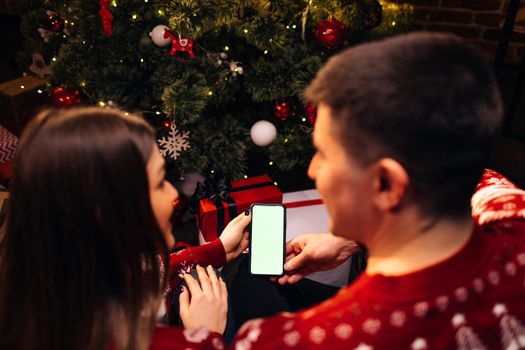 Caucasian couple using smartphone for christmas video call with green mock up screen. Christmas, festivity and communication technology.