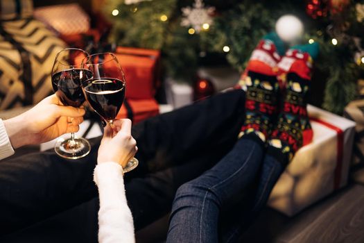 Adults people pouring wine into glasses for christmas and new year celebrations. Happy couple clink wine glasses toast and celebrate together New 2022 Year at home near glowing Christmas tree