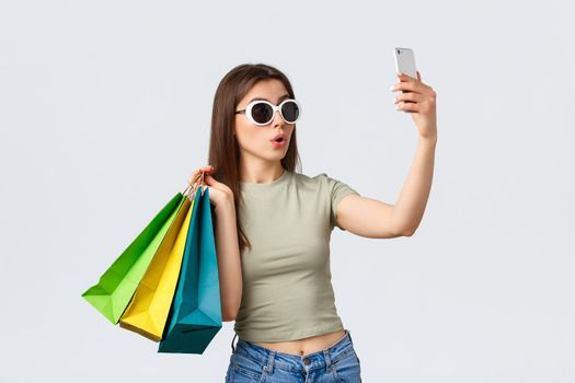 Shopping mall, lifestyle, tourism and fashion concept. Happy attractive woman tourist in sunglasses posing with shopping bags as taking selfie, buying things in favorite stores.