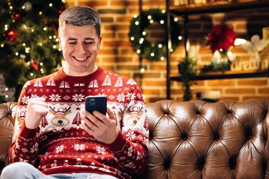 Portrait of joyful caucasian young man smiling with surprised face tapping on cell smart phone feeling excited and happy winning christmas lottery. Merry Christmas Xmas concept. Holiday miracle.