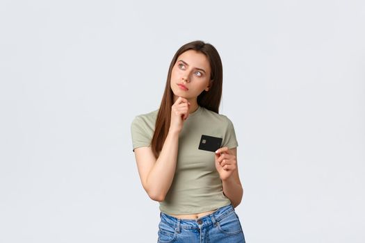 Shopping mall, lifestyle and fashion concept. Thoughtful pleased woman thinking what buy for money on bank account, looking left with pleased smile and holding credit card.