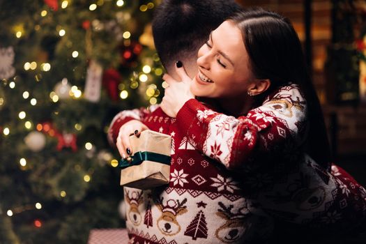 Caucasian family embracing standing near decorated glowing fir tree. Happy wife feels grateful hugs husband express gratitude for New Year gift. Christmas holidays celebration concept.