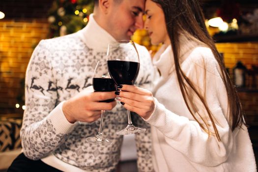 Love romance holiday celebration concept. Couple holding and drinking wine glasses sitting on sofa. Joy female and male toasting with red wine.