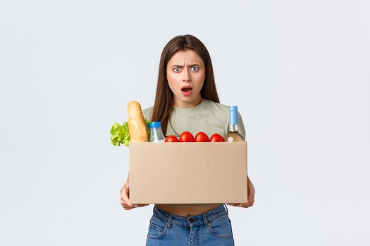 Online home delivery, internet orders and grocery shopping concept. Mad and frustated woman receive wrong order of groceries, frowning as open box with products, standing white background.