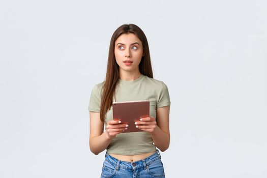 Fashion and beauty, lifestyle and shopping concept. Thoughtful attractive woman in casual outfit looking away, thinking what buy in online store using digital tablet,white background.