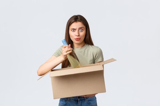 Online home delivery, internet orders and grocery shopping concept. Confused woman open box with internet order of groceries, take-out wine bottle and look puzzled, received wrong products.