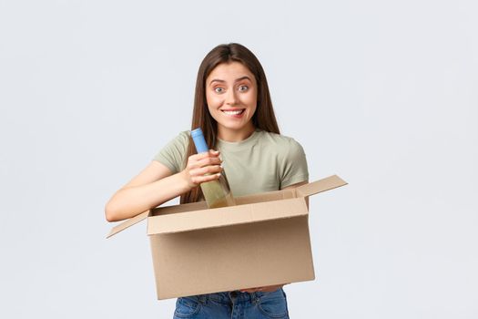 Online home delivery, internet orders and grocery shopping concept. Excited woman ordered groceries in internet store, holding box take-out bottle of wine and smiling amused.