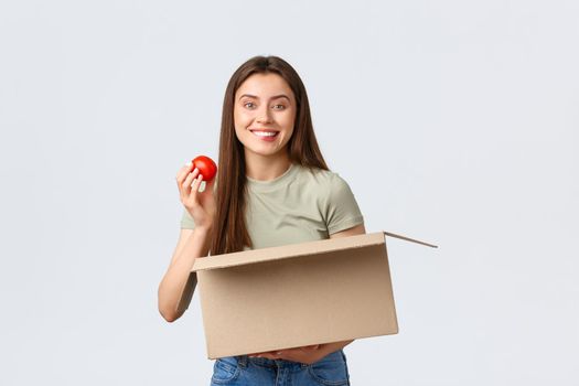 Online home delivery, internet orders and grocery shopping concept. Excited cute female customer receive groceries from internet store, take-out tomato and smiling satisfied.