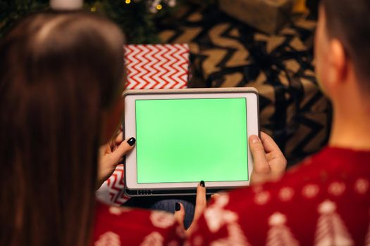 Hands holding a tablet computer with green mock up screen. Caucasian couple using tablet for christmas video call with happy couple on screen. Christmas, festivity and communication technology.