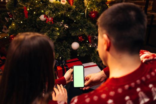 Couple using smartphone for christmas video call with green mock up screen. Christmas, festivity and communication technology. Hands holding a smart phone with green mock up screen.