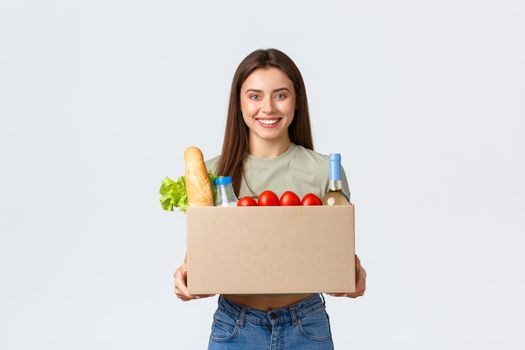 Online home delivery, internet orders and grocery shopping concept. Smiling satisfied female customer receive box with groceries from courier, standing white background.