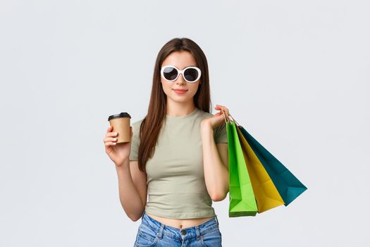 Shopping mall, lifestyle, tourism and fashion concept. Stylish carefree woman in sunglasses, drinking coffee and purchase clothes, holding takeaway cup and shop bags.