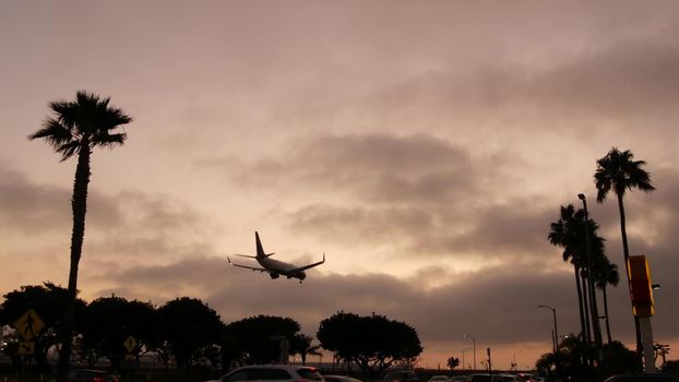 Airplane landing in airport at sunset, Los Angeles, California USA. Passenger flight or cargo plane silhouette, dramatic cloudscape. Aircraft arrival to airfield. International transport flying.