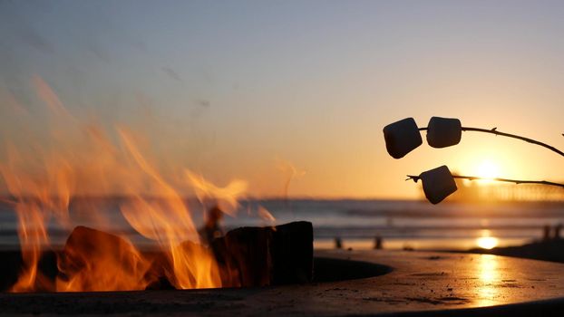 Campfire pit by Oceanside pier, California USA. Camp fire on ocean beach, bonfire flame in cement ring place for bbq, sea water waves. Heating, roast or toast marshmallow on stick. Romantic sunset sky