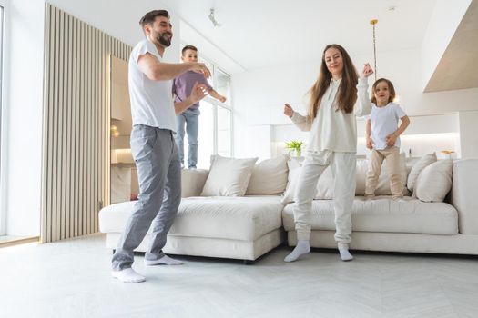 Family having fun at home. Married couple with little kids dancing moving in living room. Happy family spend time together concept