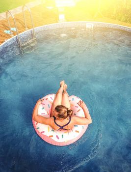 Summer warm vacation.The girl sits on a rubber ring in the form of donut in blue pool in the sun.Time to relax on an air mattress. Having fun in the water for a family vacation.Sea resort.Copy space.