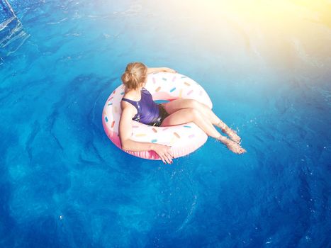 Summer warm vacation.The girl sits on a rubber ring in the form of donut in blue pool in the sun.Time to relax on an air mattress. Having fun in the water for a family vacation.Sea resort.Copy space.