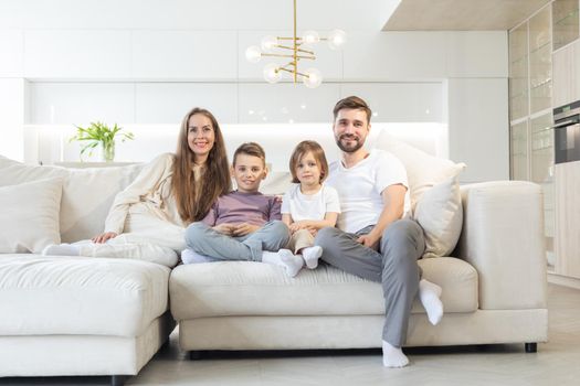 Family portrait of young parents with their two children at home, white modern desgin of living room