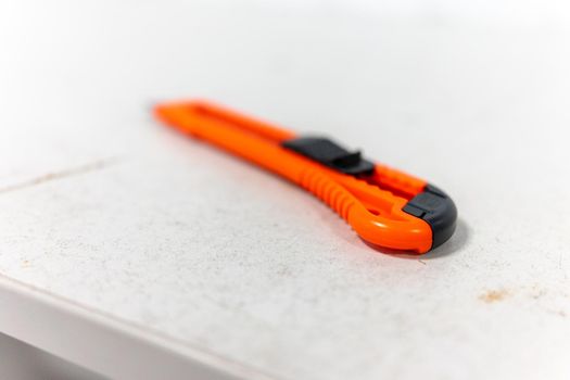 A red stationery knife lies on a white desk.