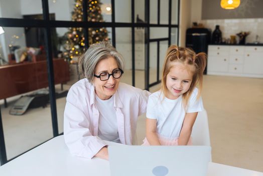 Child and granny looking at the camera with laptop at home