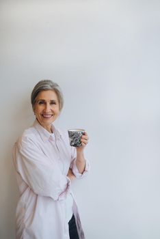 Portrait of elderly female in casual casual wear holding a mug in her hands on an isolated white background. Emotional face.