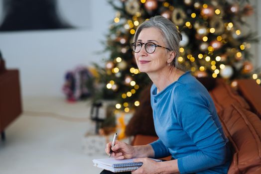 Happy senior woman in glasses writing to notebook or diary at home